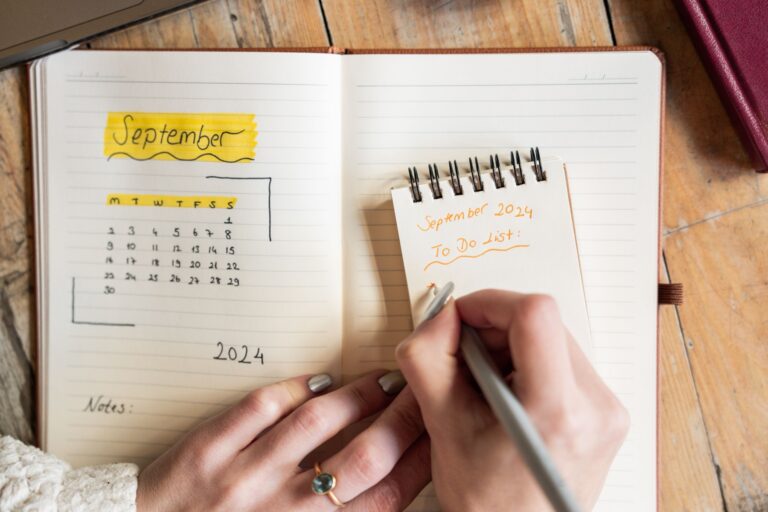 Person writing a monthly plan in a notebook and calendar