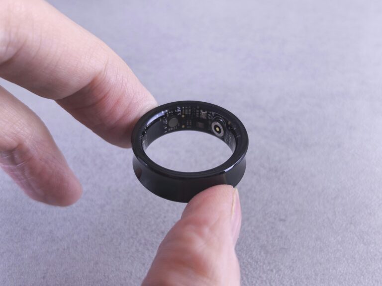 Black smart ring held between two fingers with its internal sensors visible