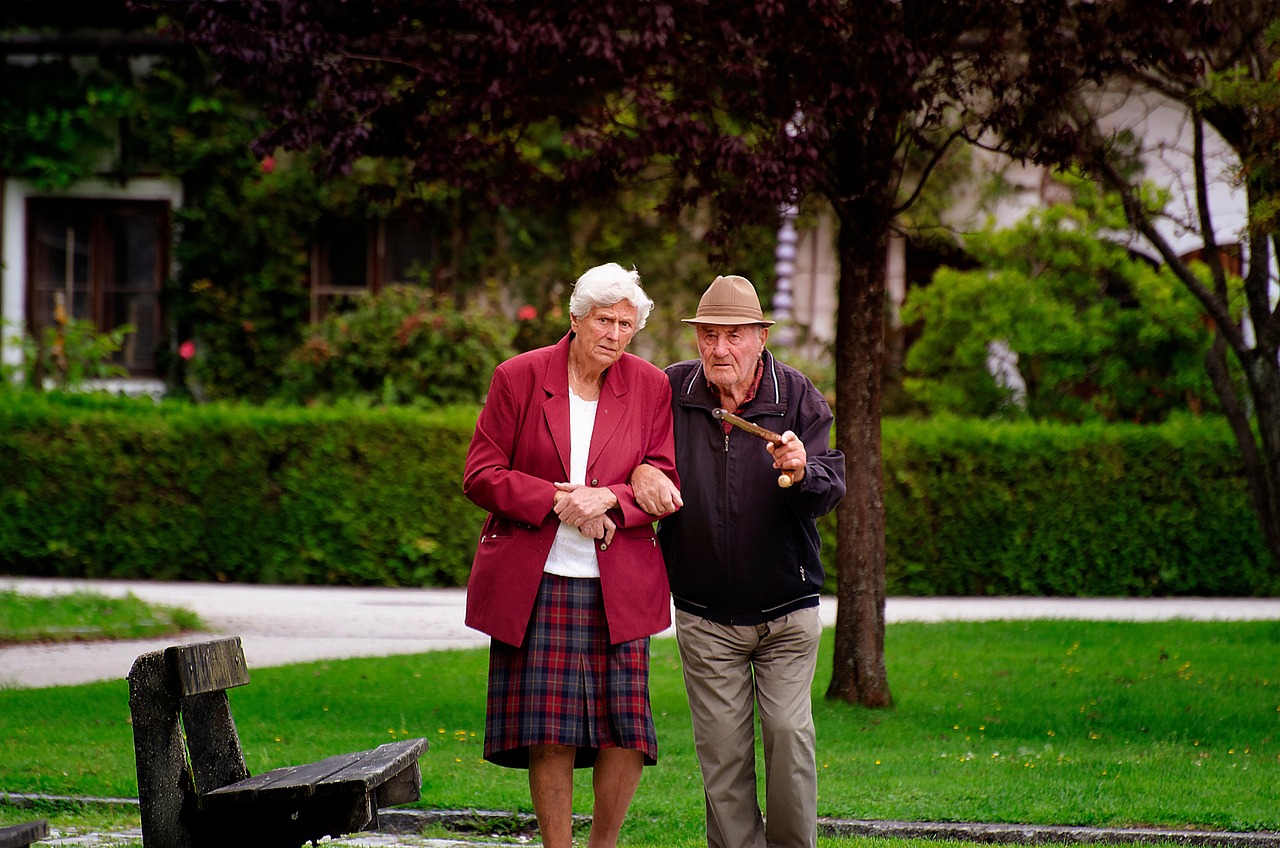 Older couple walking arm in arm through a green park