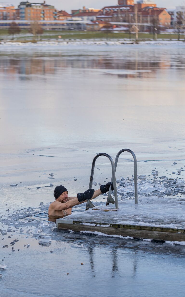 Man holding a ladder during a cold-water swim in a frozen lake